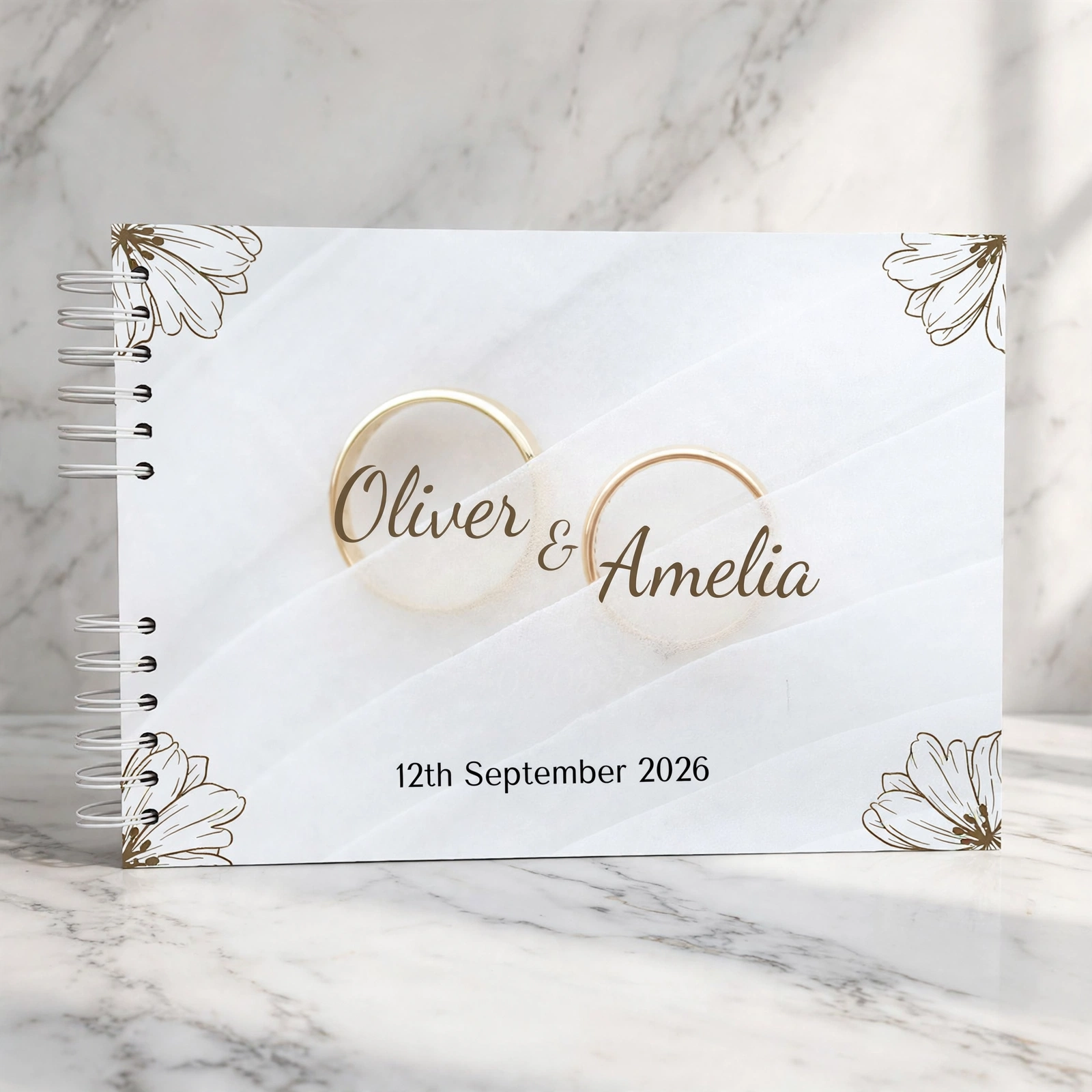 Elegant white wedding guestbook with gold line flowers, gold rings and the names Oliver & Amelia